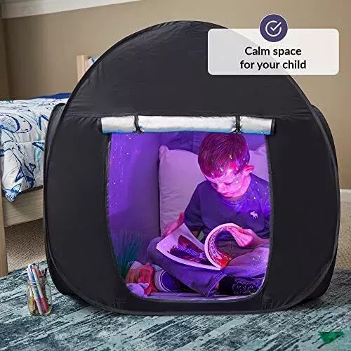 Boy is shown inside black sensory tent reading a book with purple sensory light